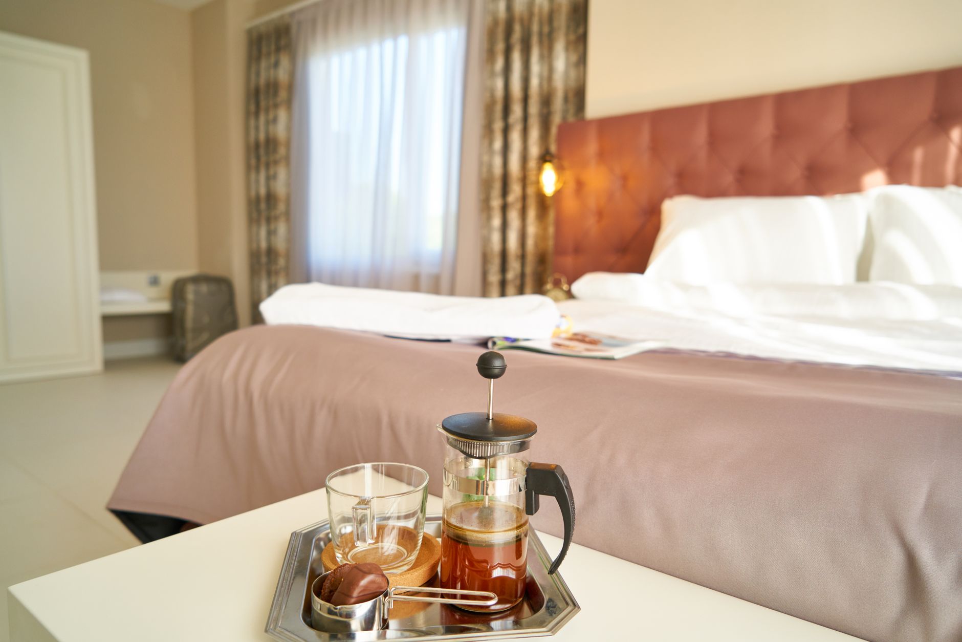 A narrow bedroom table holding a kettle, a small tray and a single mug in morning light
