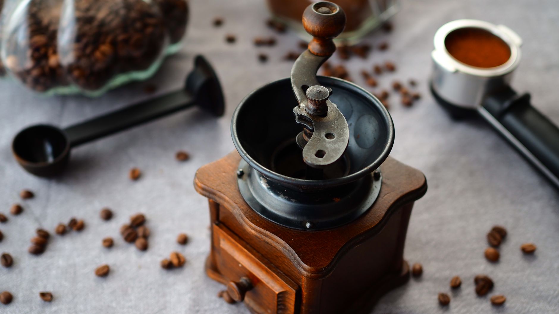 Burr grinder beside a scoop of whole coffee beans on a stone countertop