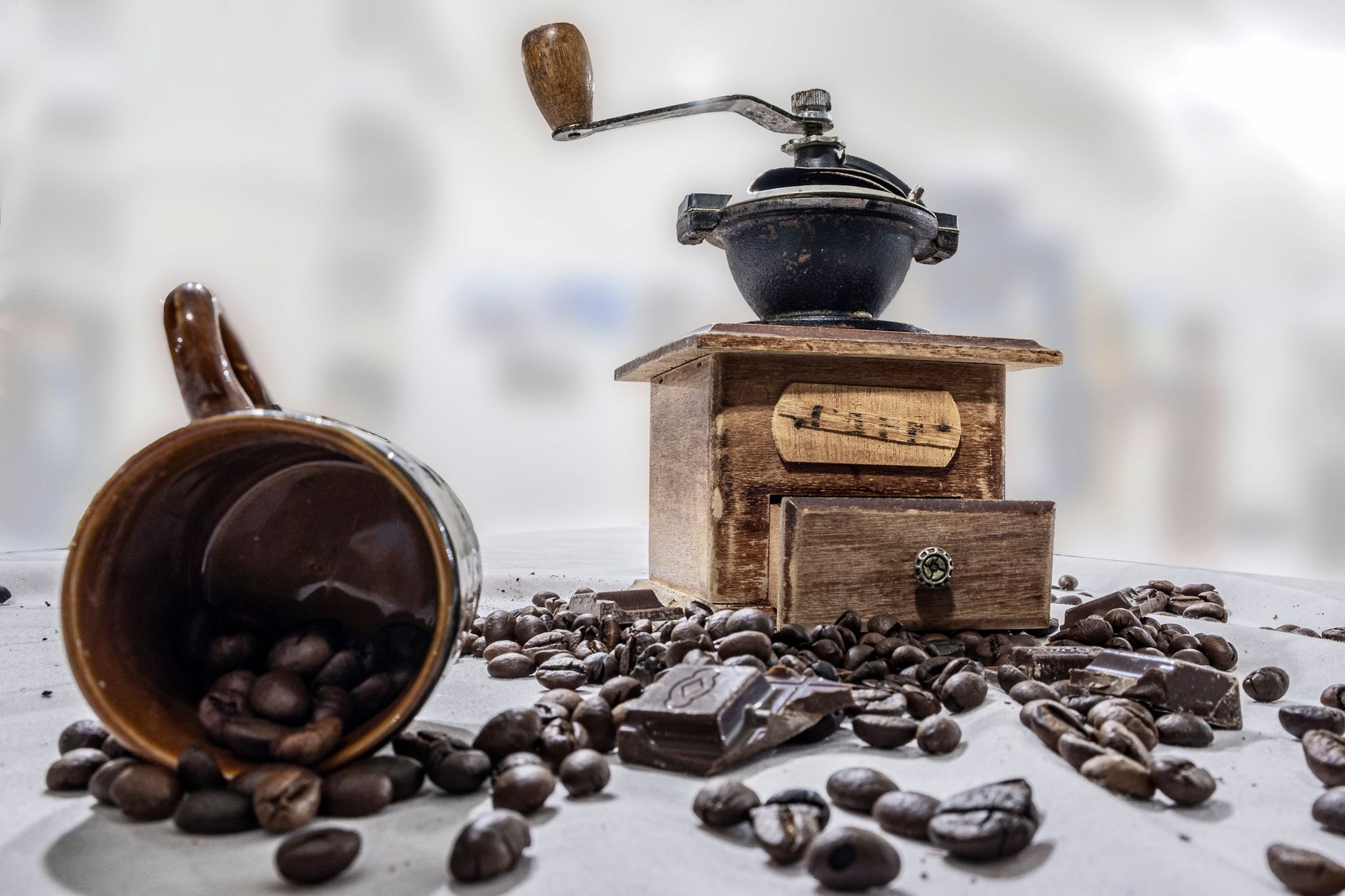 A burr grinder sitting on a dark mat with loose beans scattered around its base