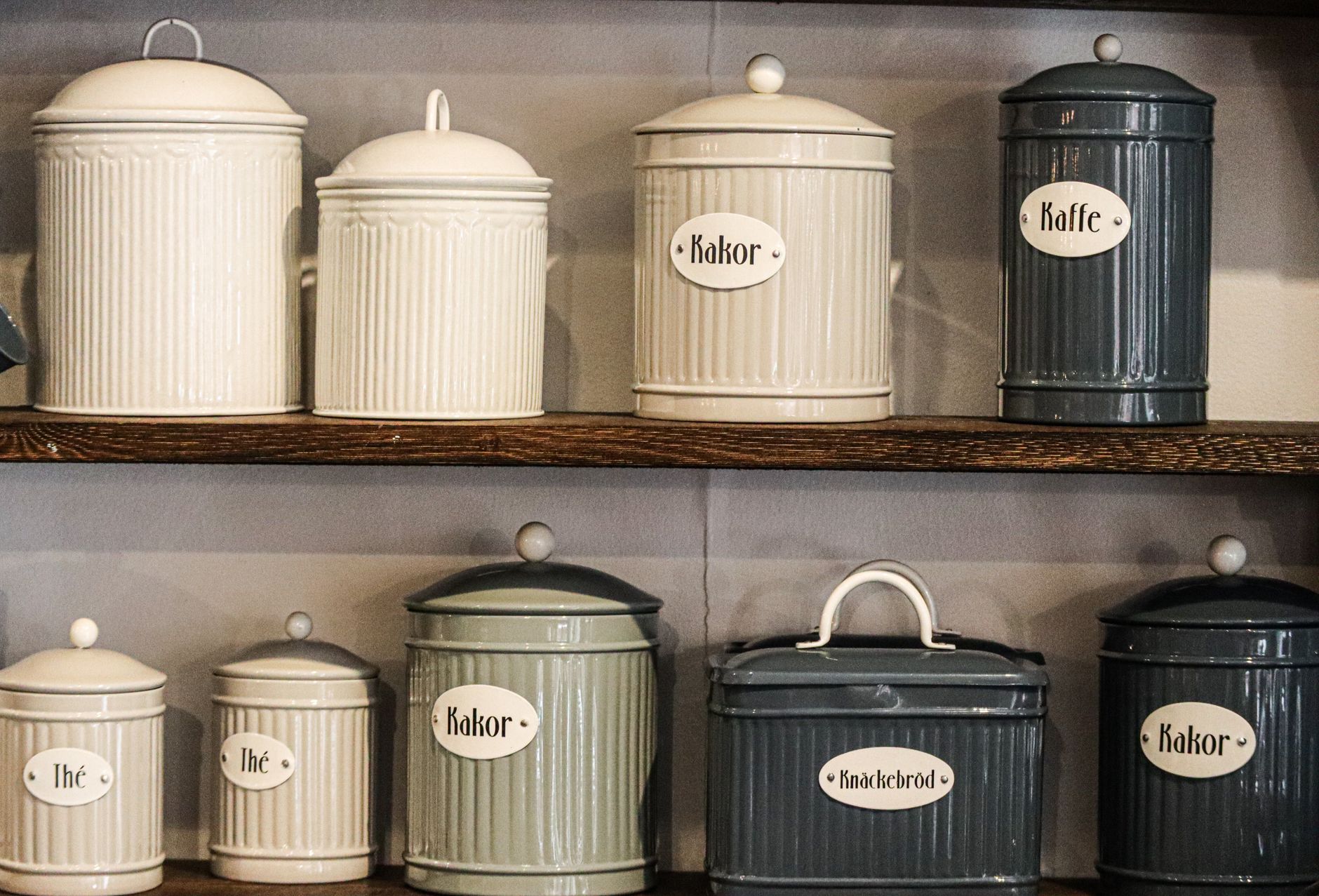 Matching canisters with small lid labels lined up on an open wooden shelf