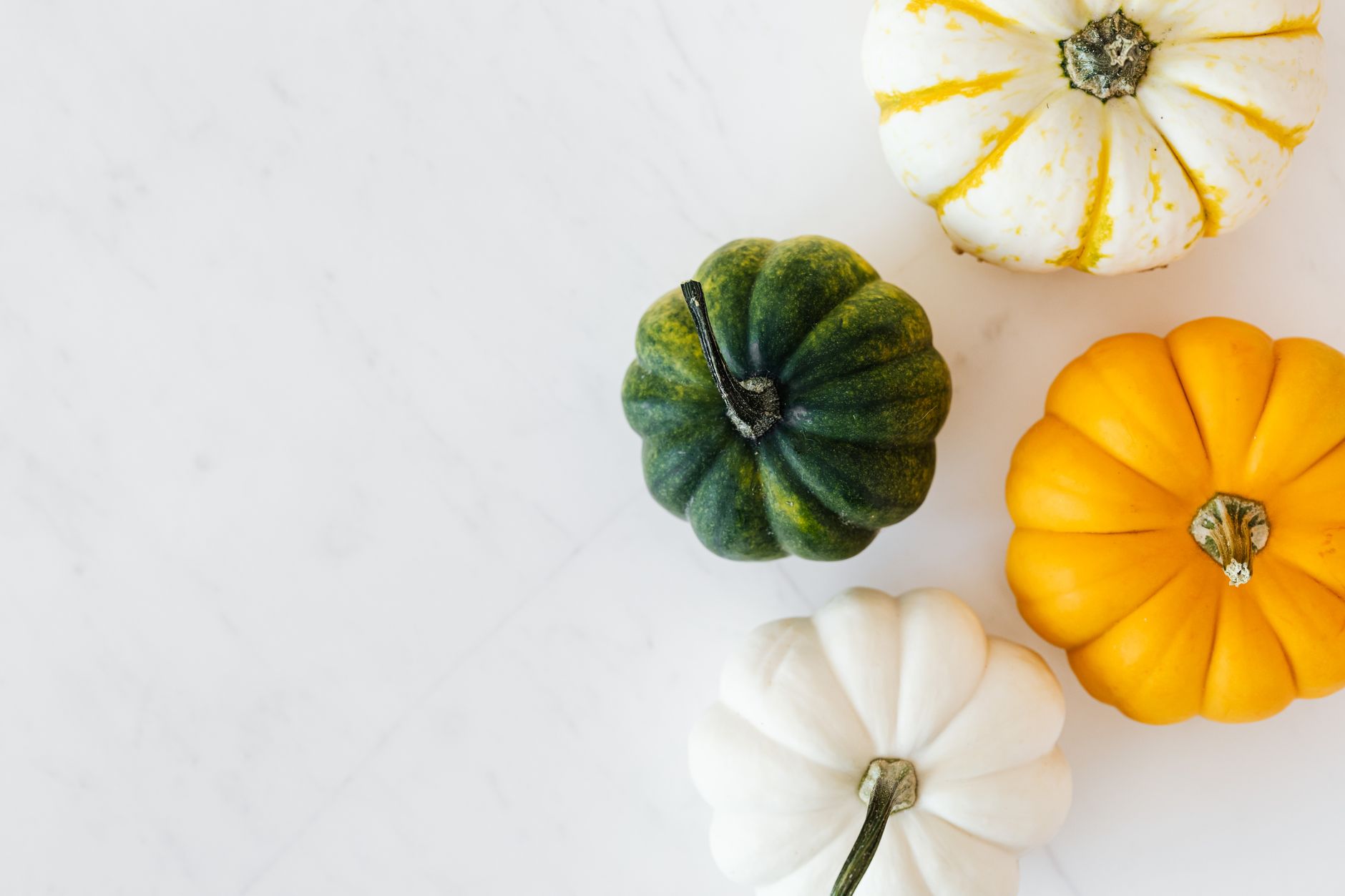Three small white pumpkins clustered at the end of a kitchen counter